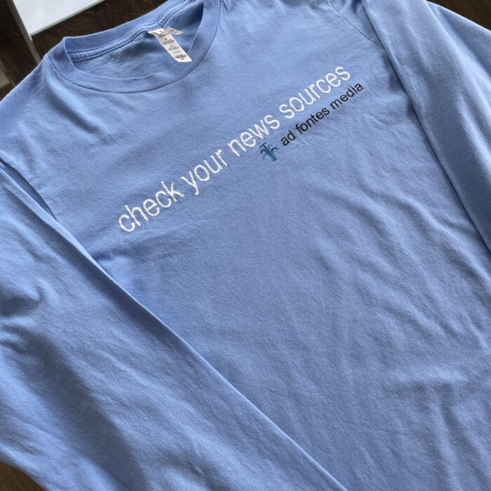 Carolina blue long-sleeved T-shirt with "Check Your News Sources," and the Ad Fontes logo.